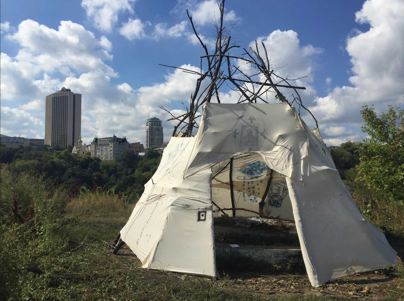 Tent constructed of sticks and fabric with high rise in background