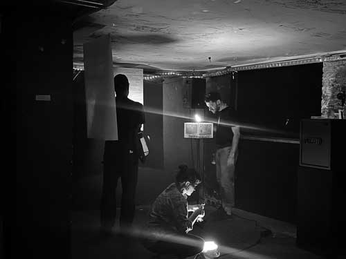 Three people in dark room looking at objects and papers