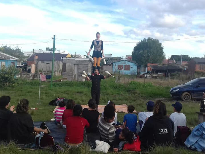Group of people sitting on the ground watching two women doing a circus act 