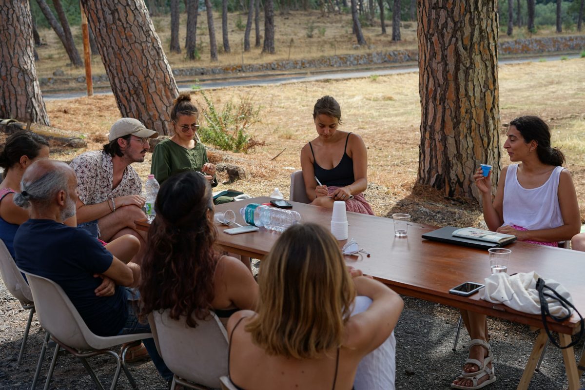 Six people sitting around a table outdoors discussing