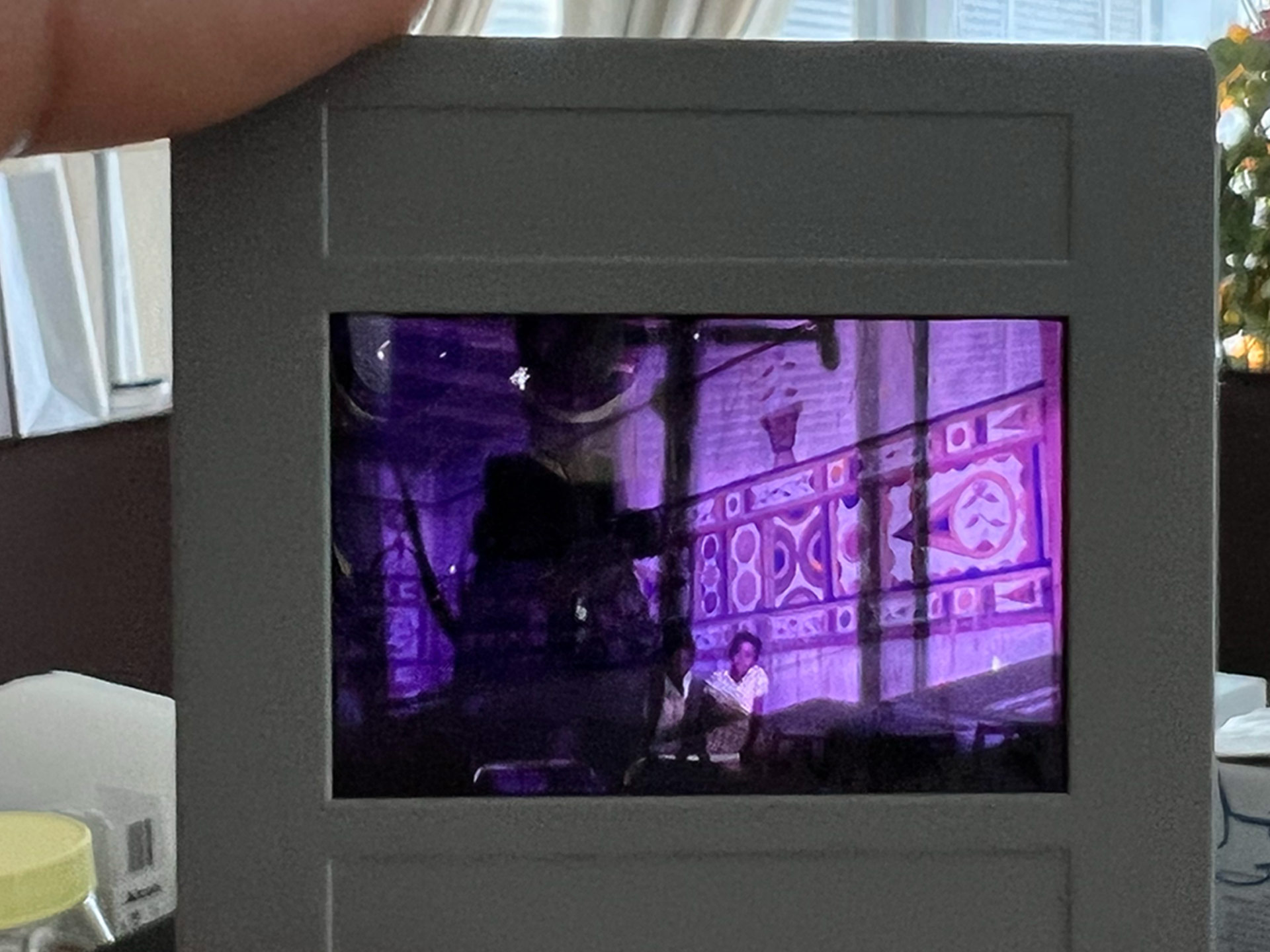 A person is holding a 35 mm slide up to a window, letting light shine through it, revealing an image of two children in a beautifully adorned home.