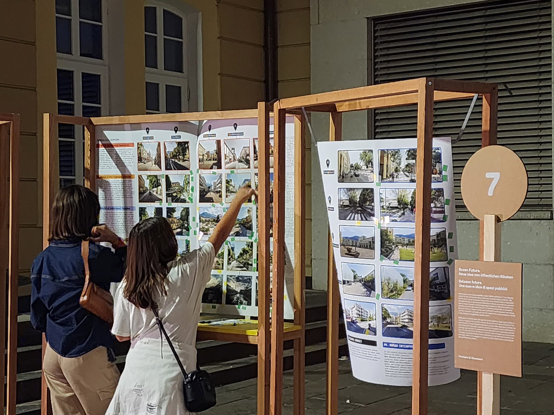 Two girls standing infron of display structure poining at a series of images with built environments