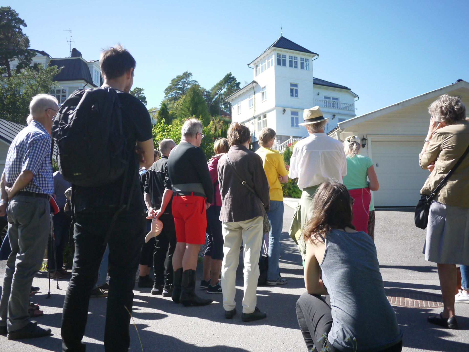 People standing in a street watching a big whilte villa
